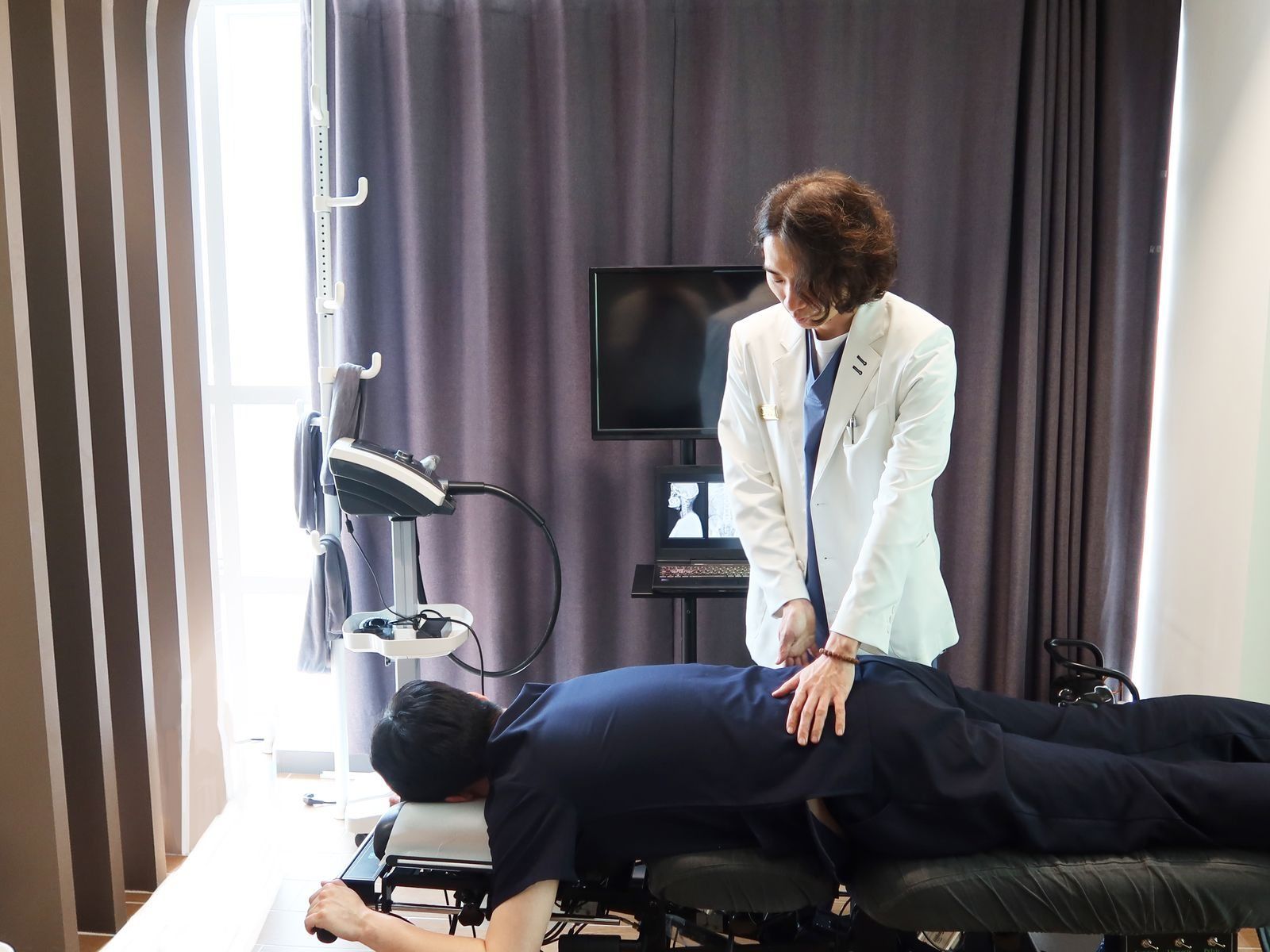 추나 치료 — 한의사가 치료대에 엎드린 분의 허리에 손을 얹고 상태를 살피는 모습