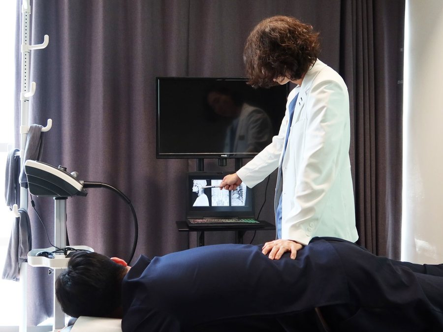 한의사가 노트북의 척추 X-ray 를 가리키며 추나 치료 부위를 설명하는 모습