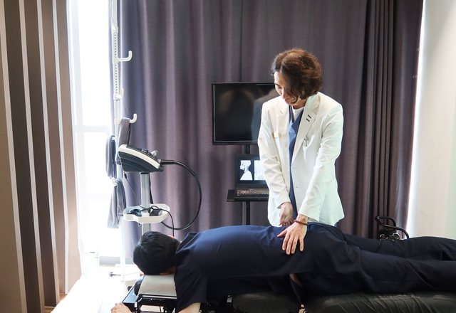 한의사가 치료대에 엎드린 환자의 허리를 손으로 추나 치료하는 모습